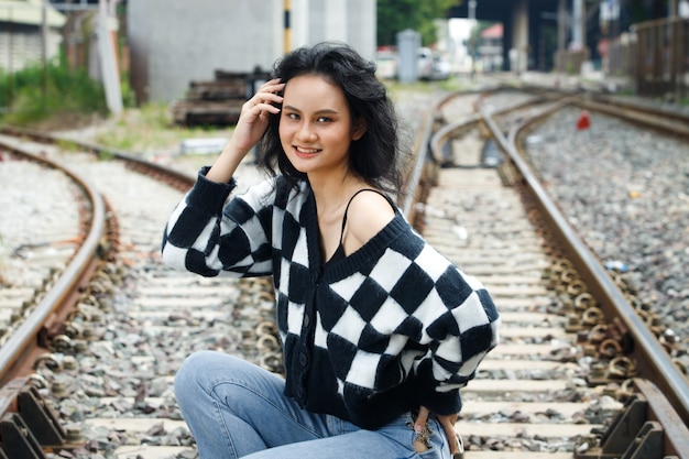 Ritratto di 20s donna asiatica capelli castani indossare giacca alta moda make up sotto la nuvola del cielo blu. La bella femmina esprime la sensazione di emozione sorridere felice sopra la stazione ferroviaria del binario del treno