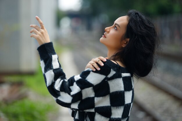 Ritratto di 20s donna asiatica capelli castani indossare giacca alta moda make up sotto la nuvola del cielo blu. La bella femmina esprime la sensazione di emozione sorridere felice sopra la stazione ferroviaria del binario del treno