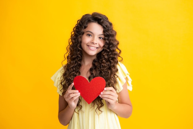 Ritratto di adolescente felice Bella ragazza adolescente romantica tenere cuore rosso simbolo dell'amore per San Valentino isolato su sfondo giallo Ragazza sorridente