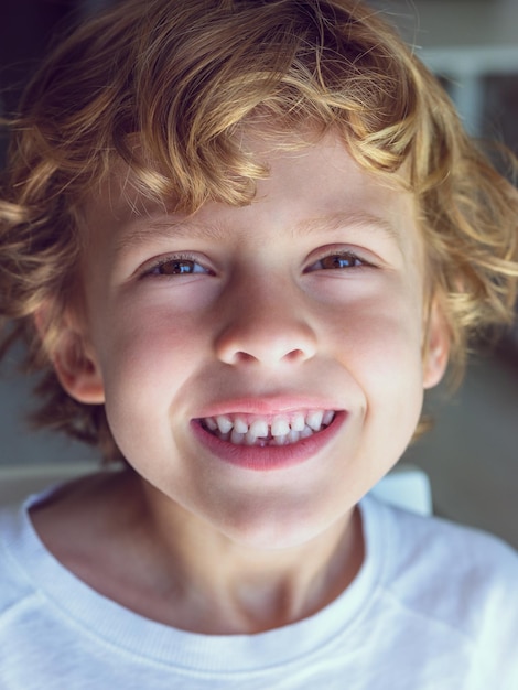 Ritratto di adorabile bambino con capelli biondi ondulati e occhi marroni che guarda l'obbiettivo con un sorriso a trentadue denti