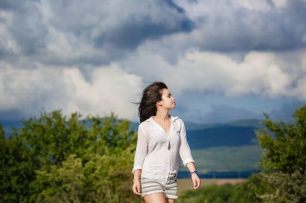 Ritratto di adorabile giovane donna in camicetta bianca e shorts in denim divertendosi all'esterno