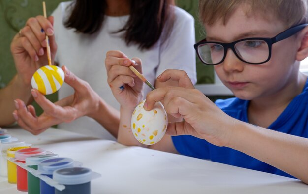 Ritratto di adorabile ragazzino che dipinge le uova di Pasqua con sua madre.