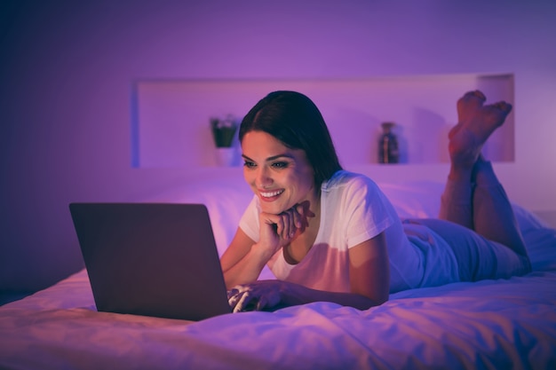 Ritratto di affascinante bella donna sdraiata sul letto utilizzando laptop a casa