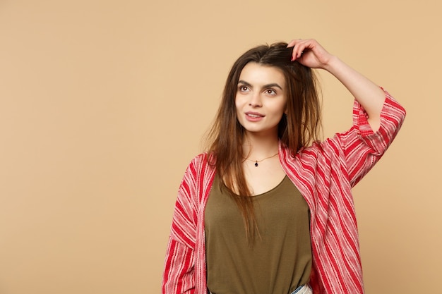 Ritratto di affascinante giovane donna in abiti casual che guarda da parte mettendo la mano sulla testa isolata sul fondo della parete beige pastello in studio. Concetto di stile di vita di persone sincere emozioni. Mock up copia spazio.