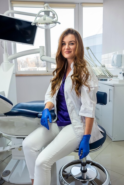 Ritratto di allegra dentista femminile in uniforme che guarda la fotocamera solo nella moderna clinica sanitaria