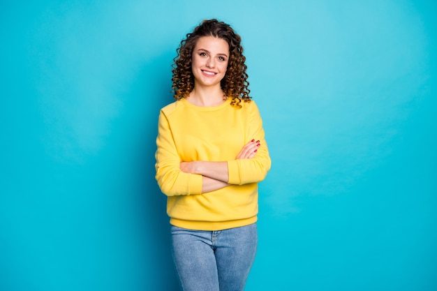 Ritratto di allegra ragazza dai capelli ondulati con le braccia piegate isolate su sfondo di colore blu