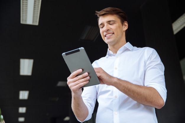 Ritratto di allegro giovane imprenditore utilizza lo smartphone e sorridente vicino al centro business