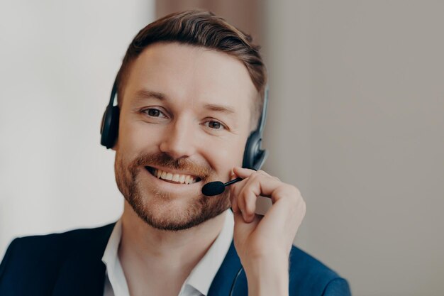 Ritratto di allegro manager maschio che indossa l'auricolare e parla alla riunione virtuale durante la consulenza del cliente in videochiamata uomo d'affari che sorride alla telecamera mentre lavora in ufficio Lavoro e occupazione