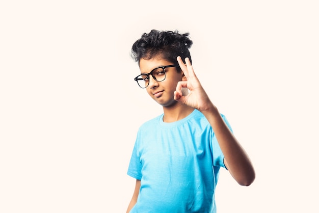 Ritratto di allegro ragazzino asiatico indiano con occhiali che celebra il successo in piedi contro il muro bianco white