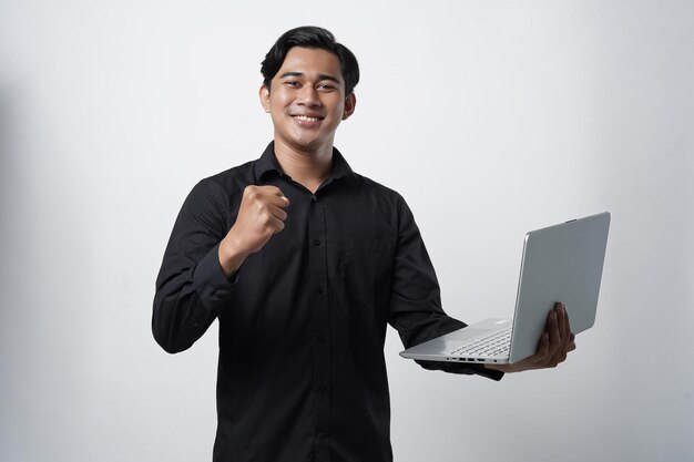 Ritratto di allegro ragazzo millenario asiatico che utilizza il laptop per lavorare online con un gesto di successo