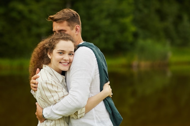 Ritratto di amare le giovani coppie che abbracciano in piedi dal lago all'aperto in estate