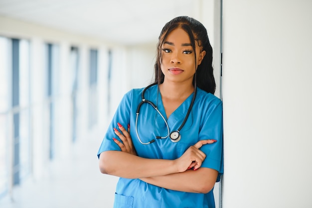 Ritratto di amichevole, sorridente fiducioso professionista sanitario femminile con camice da laboratorio, braccia incrociate tenendo gli occhiali. Fondo isolato della clinica dell'ospedale.