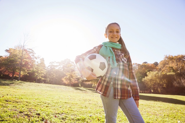 Ritratto di angolo basso del pallone da calcio sorridente della tenuta della ragazza in parco