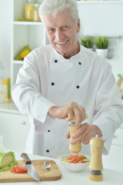 Ritratto di anziano chef maschio speziando insalata a casa