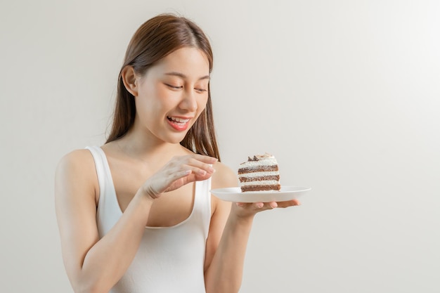 Ritratto di attraente bella ragazza asiatica giovane donna adolescente in possesso di un pezzo di torta al cioccolato emozione godere dolce dieta dieta per la perdita di peso per dimagrire sfondo bianco isolato spazio copia