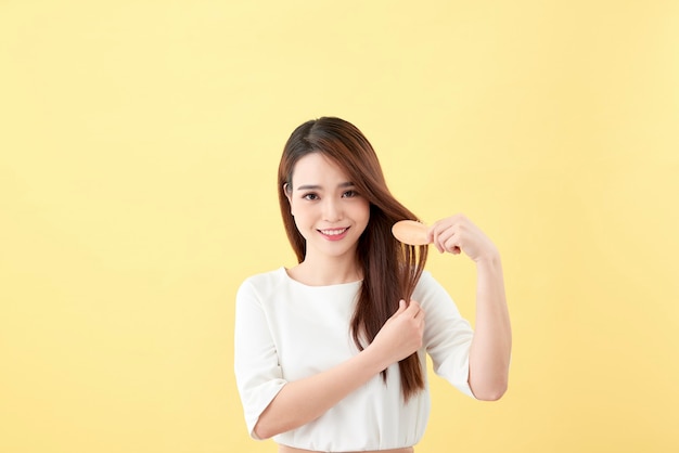 Ritratto di attraente donna sorridente che si spazzola i capelli isolati su giallo studio shot yellow