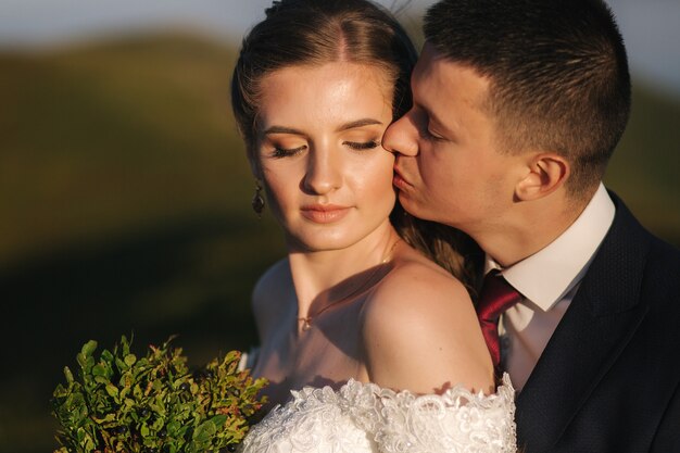 Ritratto di attraente sposa e sposo alla moda godendo momenti romantici in montagna al tramonto