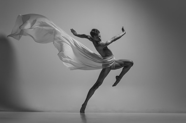 Ritratto di ballerino uomo attraente uomo flessibile che si esibisce con un panno in tessuto isolato su sfondo grigio per studio