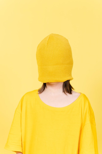 Ritratto di bambina bendata che indossa una camicia di grandi dimensioni e un cappello di lana isolato su giallo