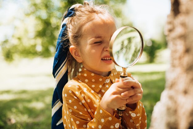 Ritratto di bambina carina che impara ed esplora la natura con la lente d'ingrandimento all'aperto Bambino che gioca con la lente d'ingrandimento Bambino curioso che guarda attraverso la lente d'ingrandimento all'albero nel parco