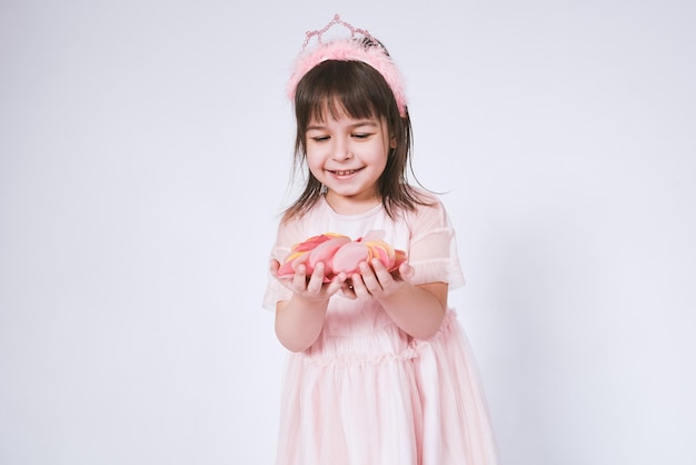 Ritratto di bambina carina che indossa un abito rosa in tulle con corona di principessa sulla testa isolata su sfondo bianco prima di soffiare i coriandoli Bella ragazza sorridente con molti coriandoli per la festa di compleanno