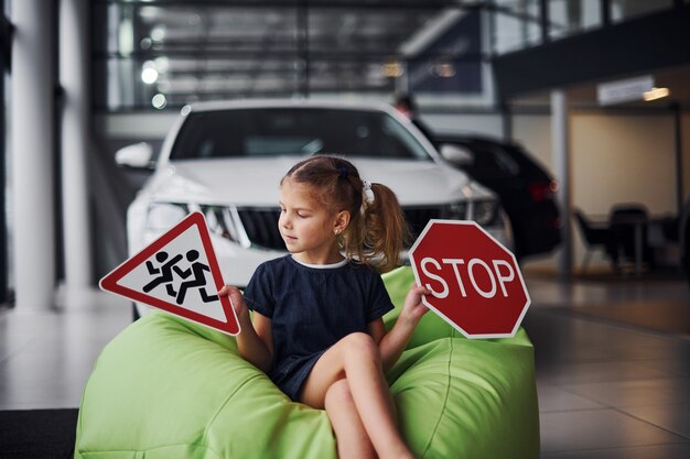 Ritratto di bambina carina che tiene in mano i segnali stradali nel salone dell'automobile.