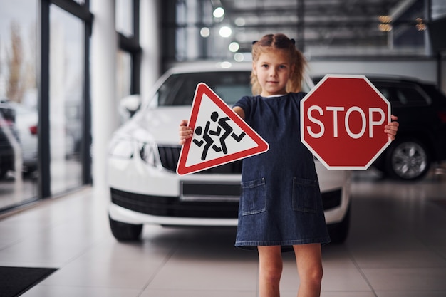 Ritratto di bambina carina che tiene in mano i segnali stradali nel salone dell'automobile.