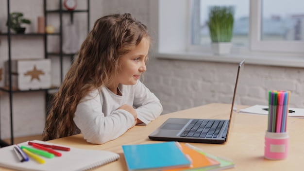 Ritratto di bambina carina felice godendo il suo cartone animato preferito su un computer portatile. Ragazzo sorridente della scuola primaria che guarda video sul computer.