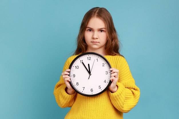 Ritratto di bambina che tiene grande orologio da parete in mano guardando la fotocamera con espressione seria
