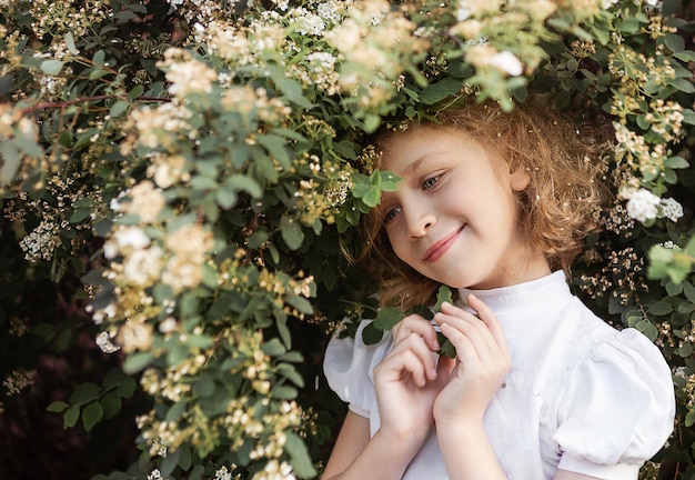 Ritratto di bambina con lunghi capelli biondi, close up, cespuglio fiorito. Concetto di tempo di primavera.