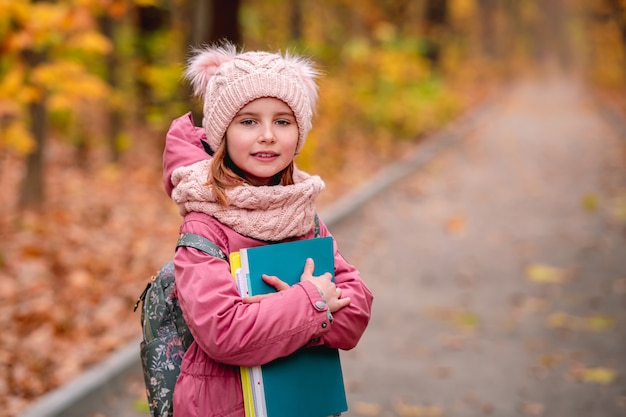 Ritratto di bambina con zaino tenendo le cartelle mentre si sta in piedi sulla strada del parco in autunno