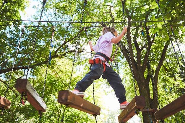 Ritratto di bambina coraggiosa a piedi su un ponte di corda in un parco avventura corda. Divertirsi al parco avventura. Scout che pratica la discesa in corda doppia