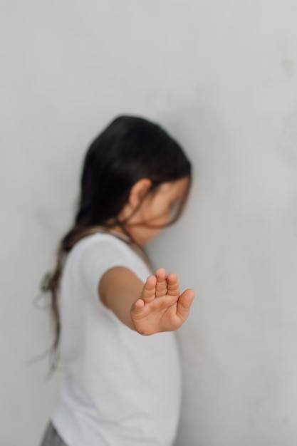 Ritratto di bambina spaventata con i capelli lunghi in piedi di fronte al muro che allunga la mano in verticale