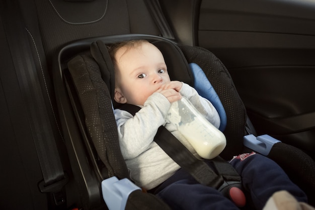 Ritratto di bambino carino che beve latte nel seggiolino per auto