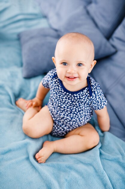 Ritratto di bambino che ride felice con gli occhi azzurri, in camicia blu, seduto sul divano.
