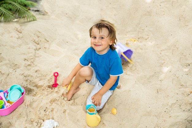 Ritratto di bambino in età prescolare seduto in una sandbox e giocare da solo con piacere. Giochi educativi all'aperto per bambini.