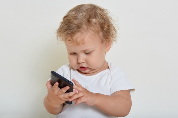 Ritratto di bambino sveglio che controlla smartphone nelle mani, studiando un nuovo soggetto sconosciuto