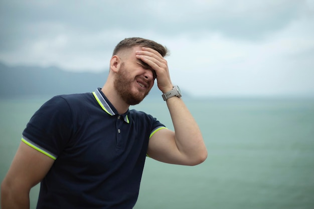 Ritratto di barbuto bello depresso sconvolto triste ragazzo frustrato giovane rimpianto su sfondo naturale oceano mare con palmo della faccia