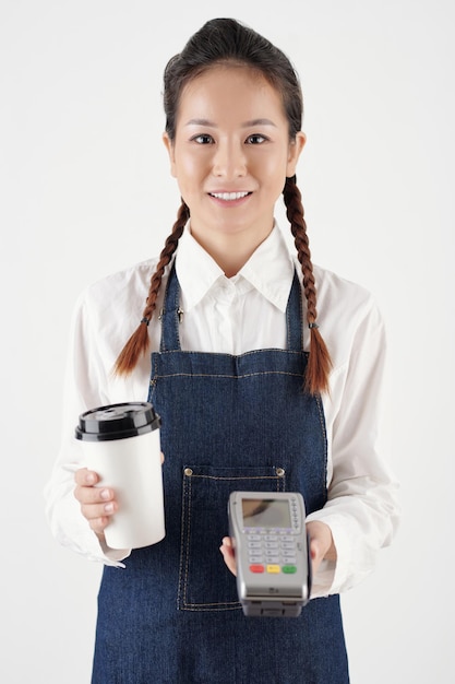 Ritratto di barista femminile sorridente che dà una tazza di caffè da asporto e terminale di pagamento