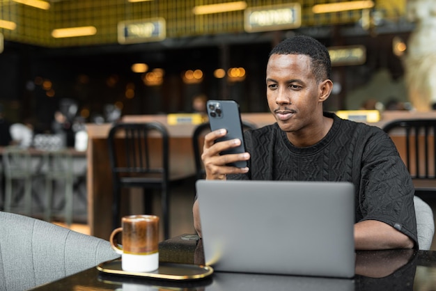 Ritratto di bel giovane africano utilizzando il computer portatile nella caffetteria