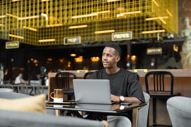 Ritratto di bel giovane africano utilizzando il computer portatile nella caffetteria