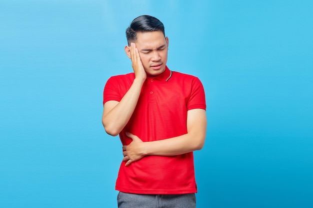 Ritratto di bel giovane asiatico in camicia rossa che sembra stordito soffre di mal di testa isolato su sfondo blu