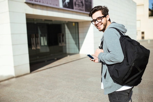 Ritratto di bel giovane che usa il suo telefono cellulare in strada.