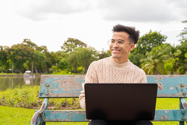 Ritratto di bel giovane nel parco durante l'estate utilizzando il computer portatile