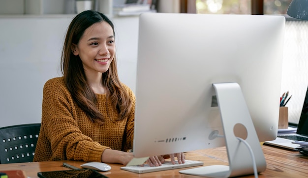 Ritratto di bel libero professionista asiatico che utilizza il computer desktop in ufficio a casa