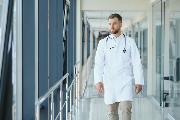 Ritratto di bel medico maschio che indossa camice bianco in piedi nel corridoio dell'ospedale