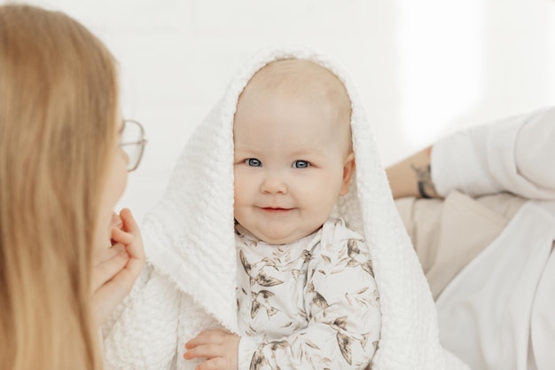 Ritratto di bel neonato paffuto dagli occhi azzurri sorridente coperto di coperta di cotone bianco seduto o