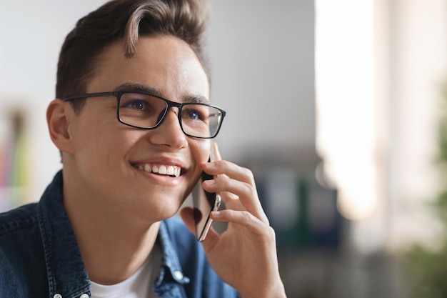 Ritratto di bel ragazzo sorridente che indossa occhiali da vista parlando al telefono cellulare