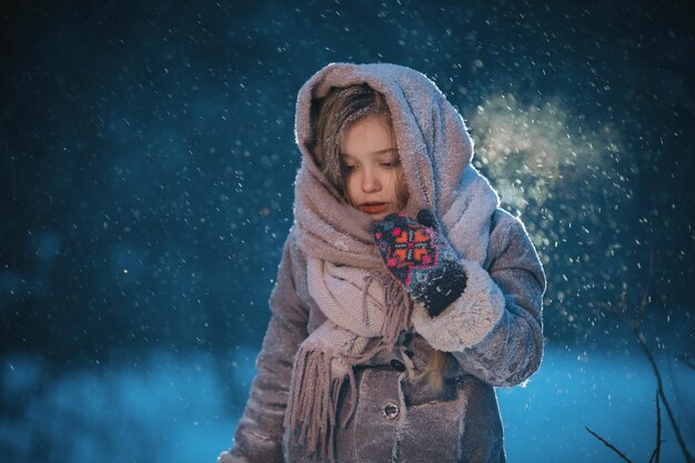 Ritratto di bella bambina carina in scialle nella foresta in inverno eveninig neve e