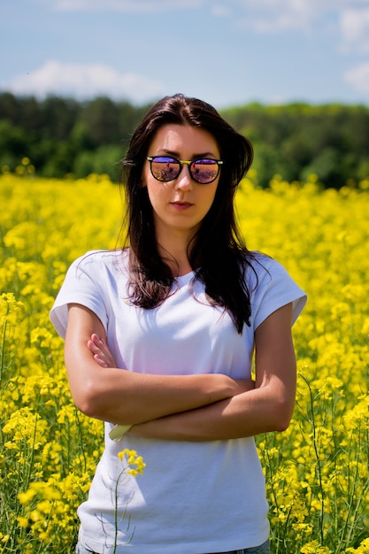 Ritratto di bella bruna in occhiali da sole, si trova nel campo di colza.